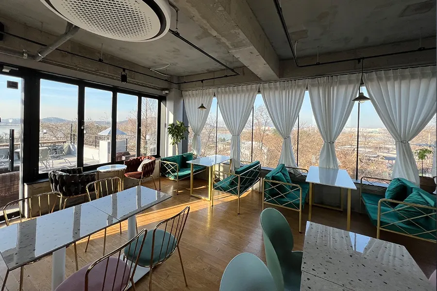 시공 전 콘크리트 인더스트리얼 인테리어의 카페 내부, 통유리로 나무들이 밝게 비치는 모습
